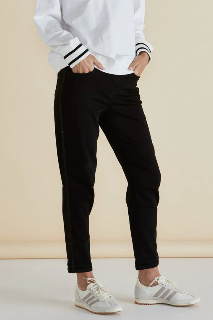 Person wearing a white sweatshirt with black stripes, black pants, and white sneakers on a beige background