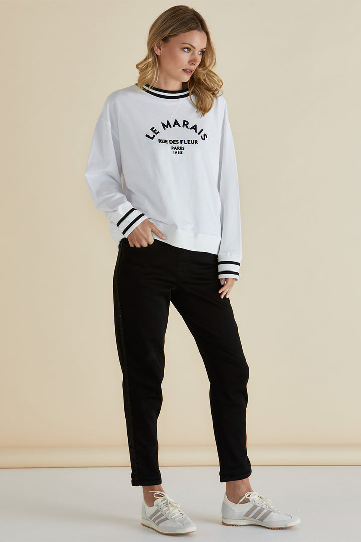 Woman wearing a white sweatshirt with text and black pants on a beige background