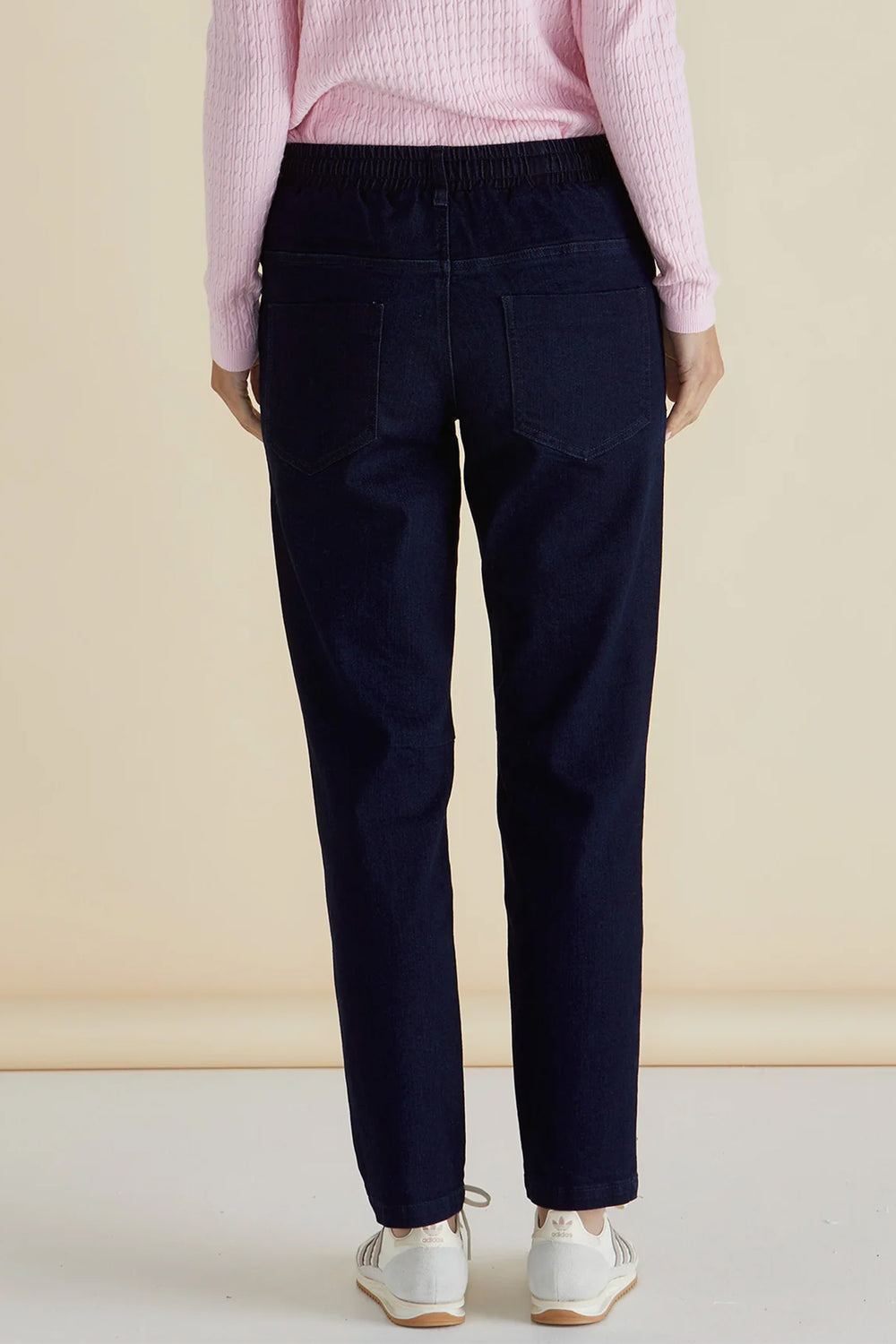 Person wearing navy pants and a pink sweater against a beige background