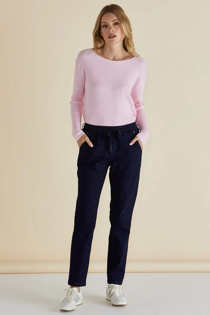 Woman wearing a pink sweater and navy pants against a beige background