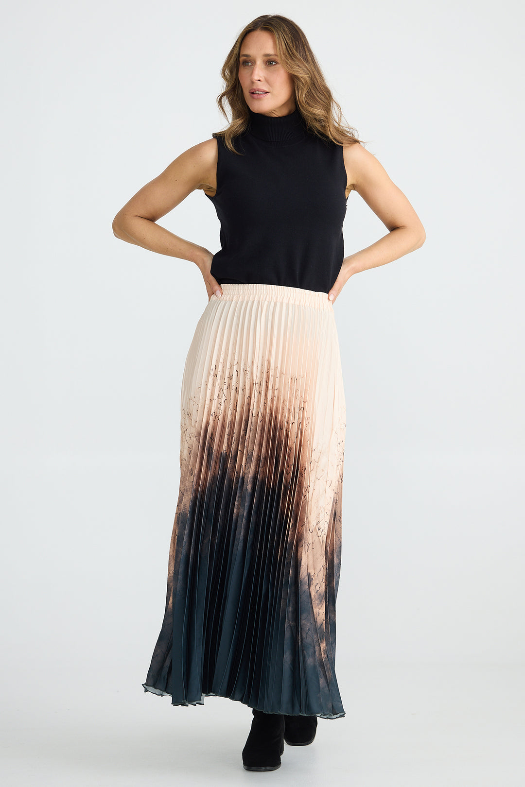 Woman wearing a black sleeveless top and a long, gradient skirt on a white background