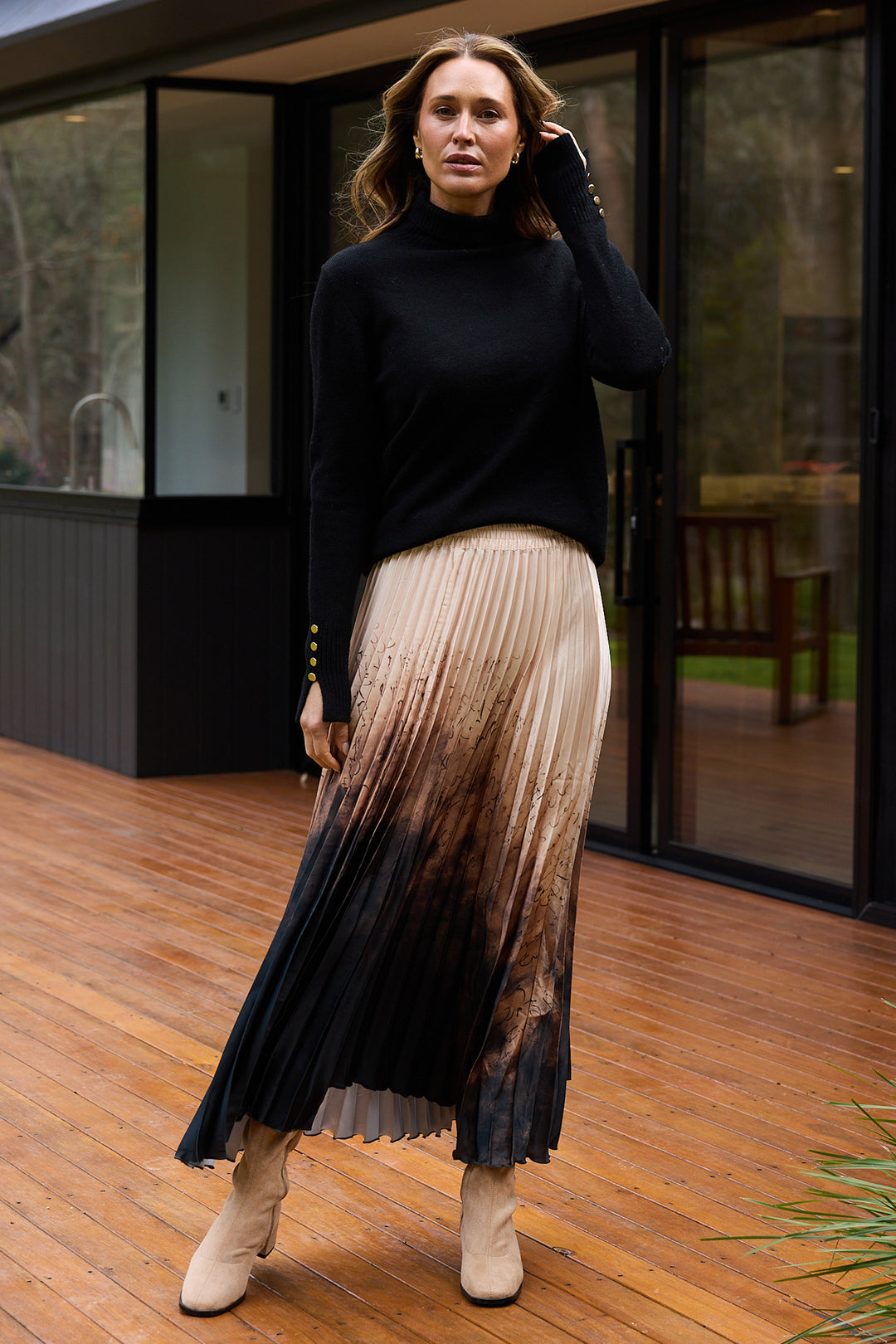 Woman wearing a black turtleneck and pleated skirt on a wooden deck.