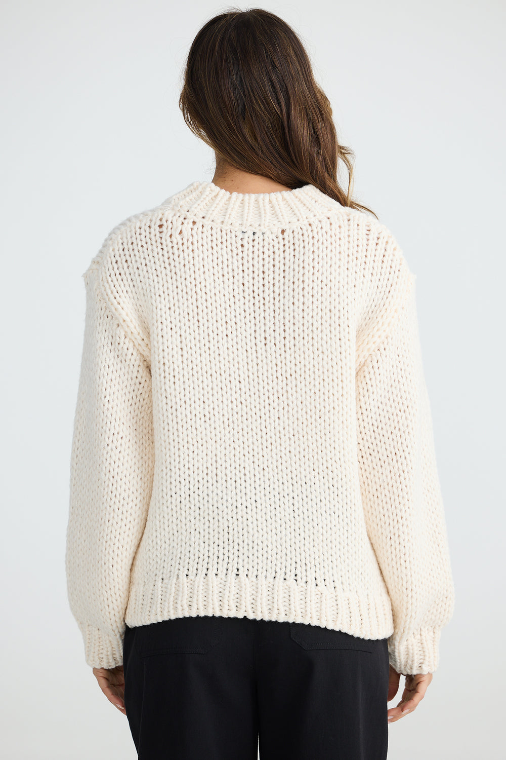Person wearing a cream knitted sweater on a white background
