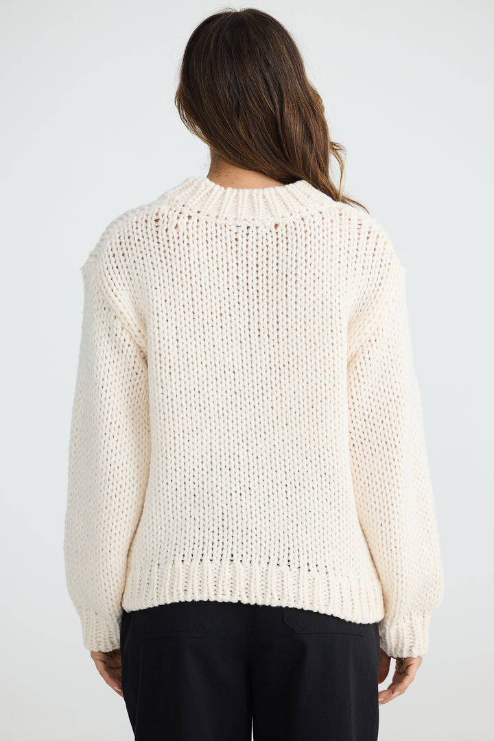 Person wearing a cream knitted sweater on a white background