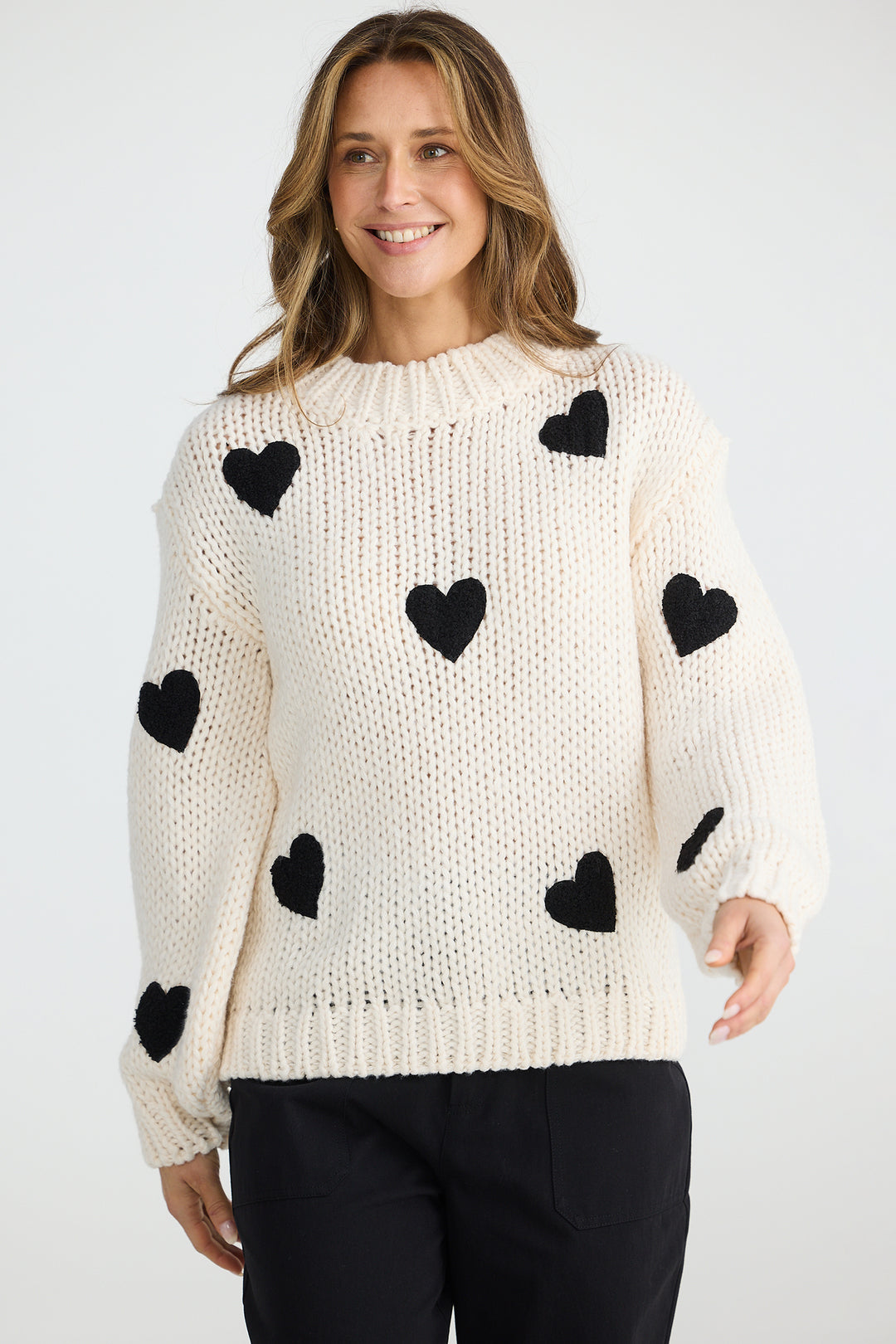 Woman wearing a cream sweater with black heart patterns on a white background