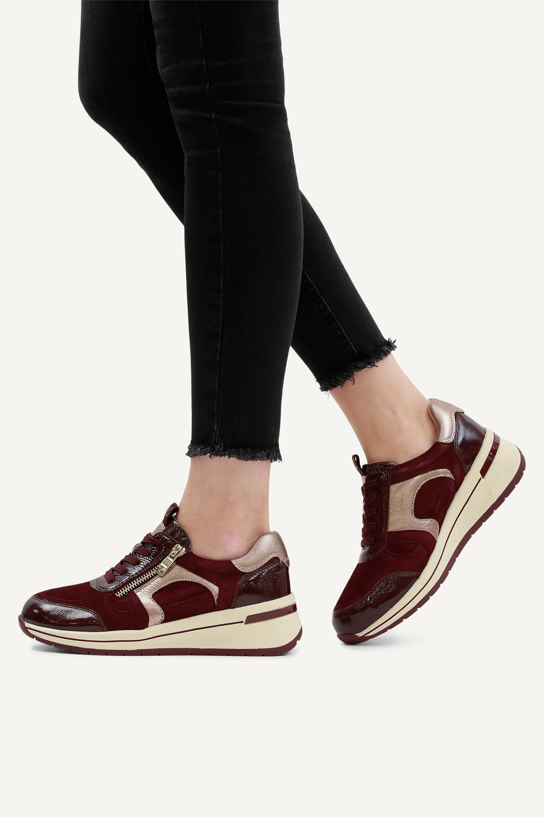 Maroon and beige sneakers worn with black pants on a white background