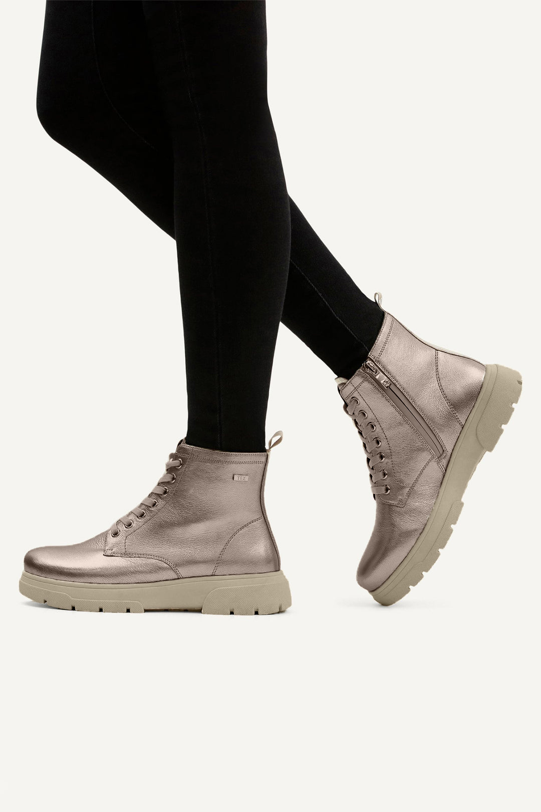 Person wearing metallic silver boots and black leggings on a white background