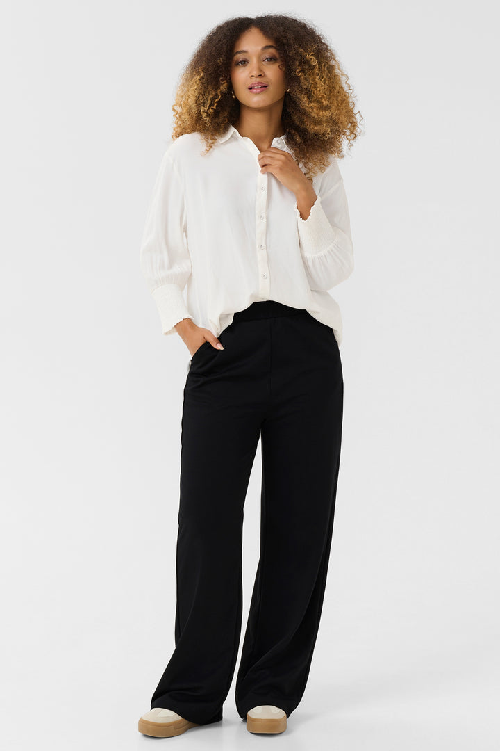 Woman wearing a white blouse and black pants on a white background