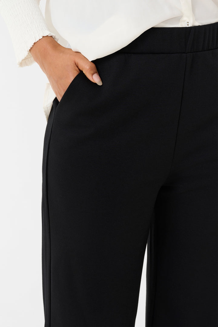 Black pants worn with a white shirt on a light background