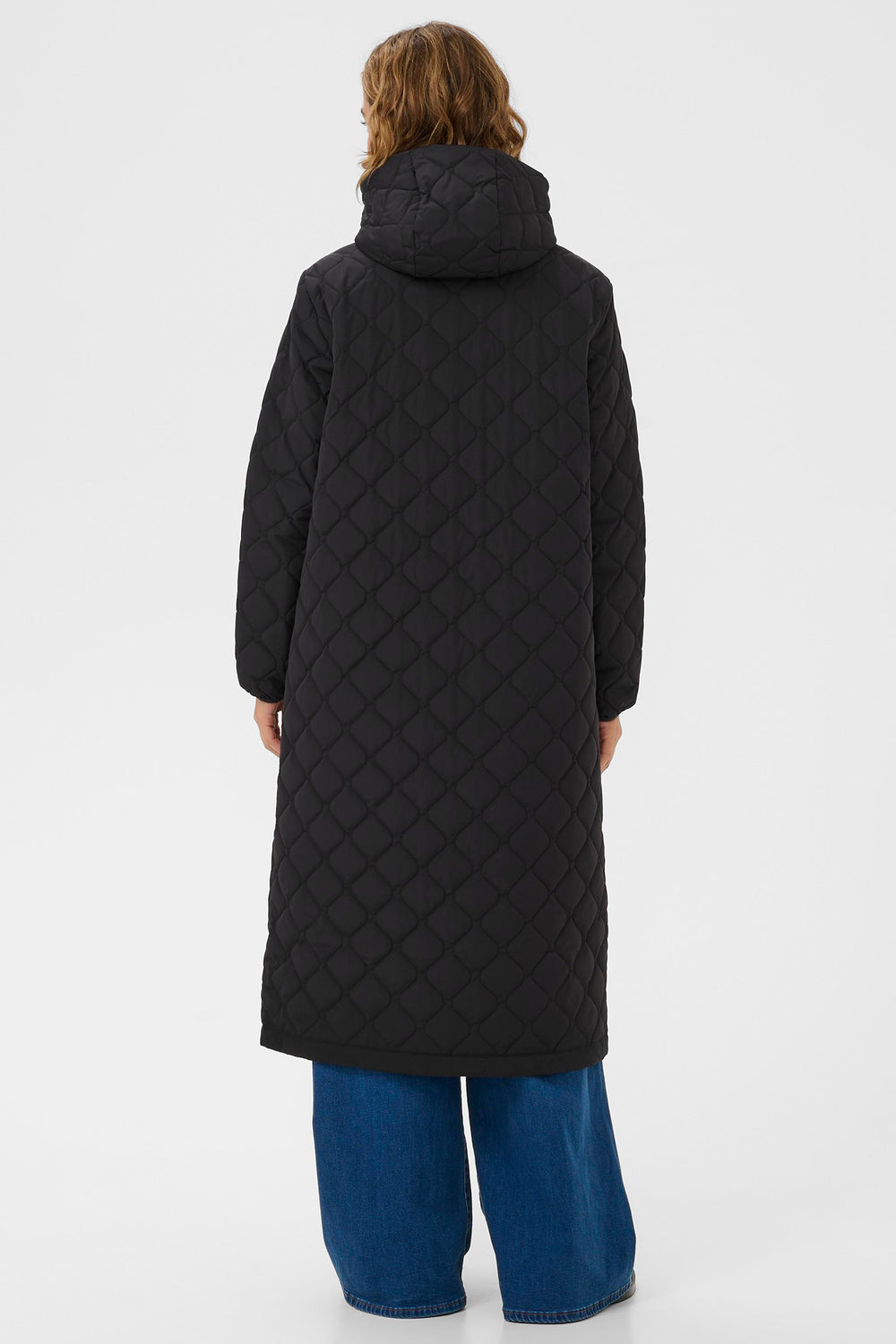 Person wearing a long black quilted coat on a white background