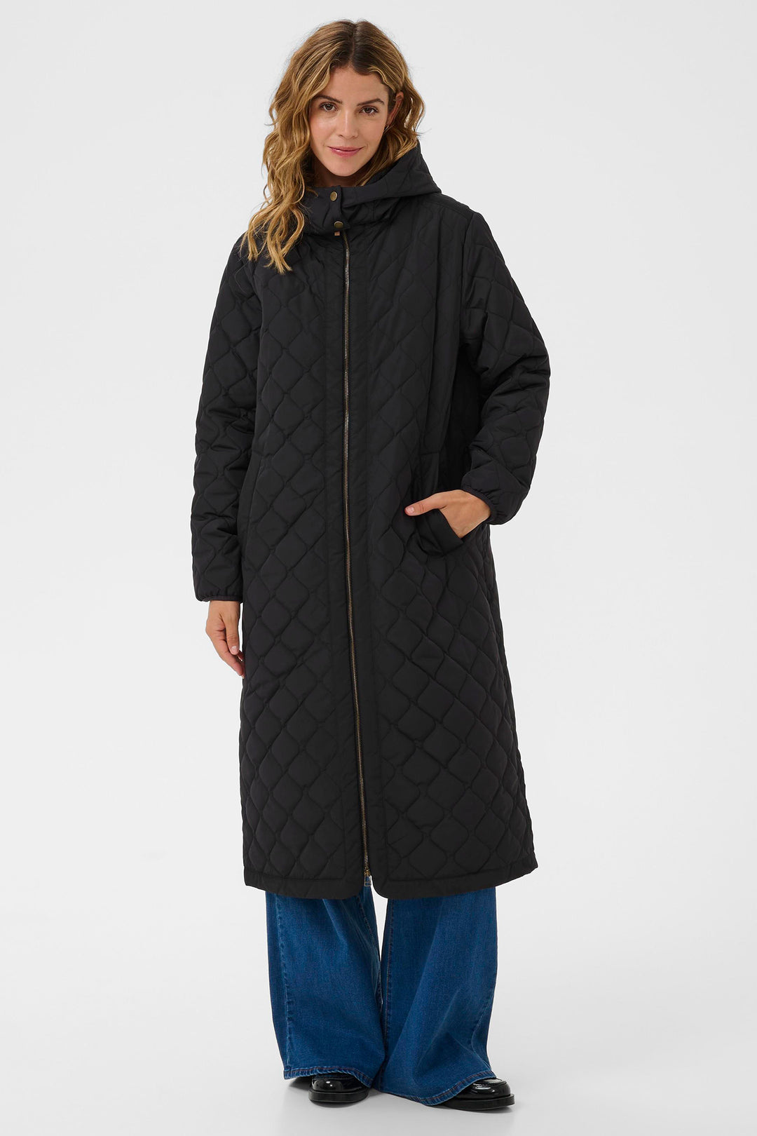 Woman wearing a long black quilted coat on a white background