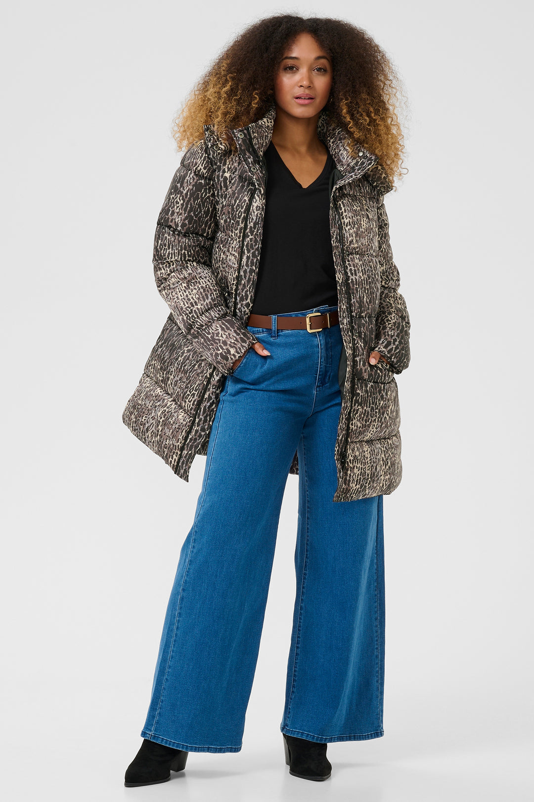 Person wearing a patterned coat, black top, blue jeans, and black shoes on a white background