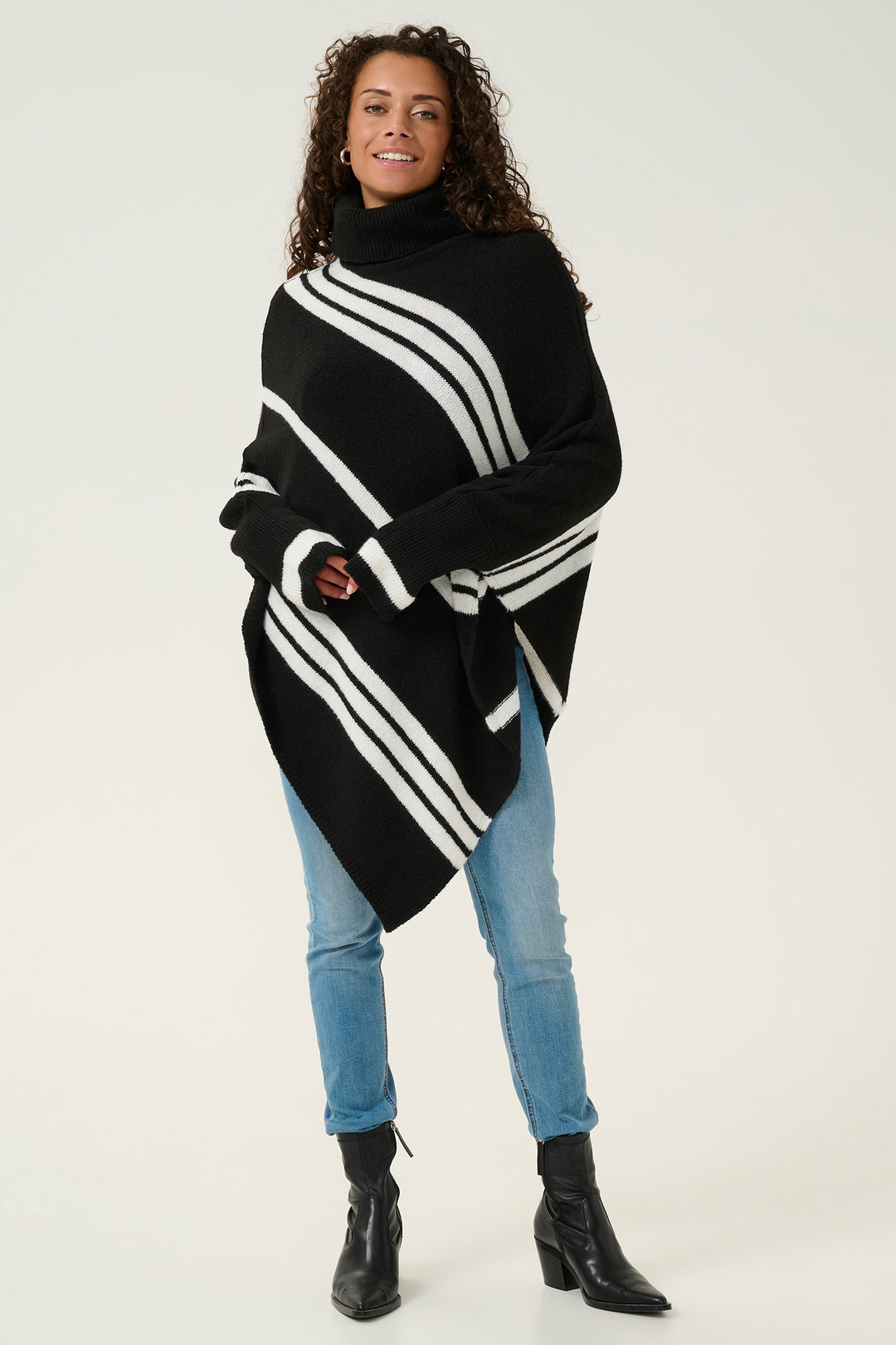 Woman wearing a black and white striped poncho with blue jeans on a white background