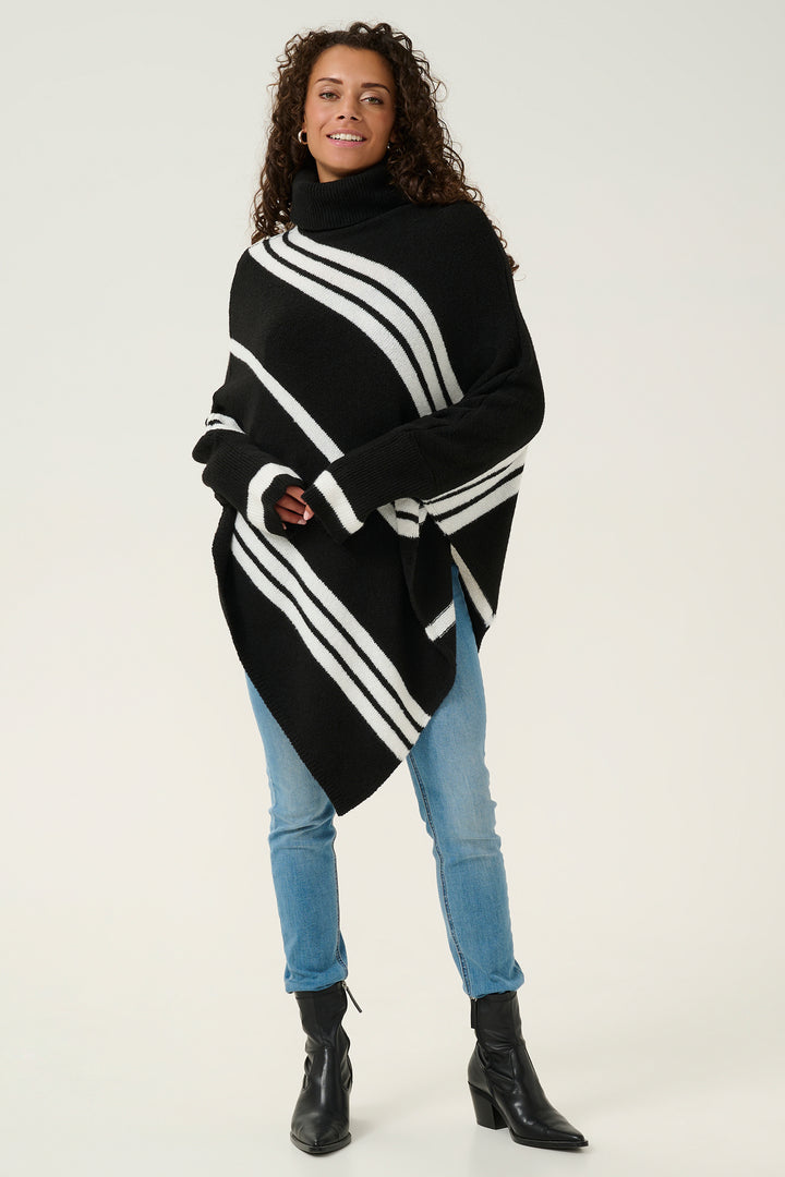 Woman wearing a black and white striped poncho with blue jeans on a white background