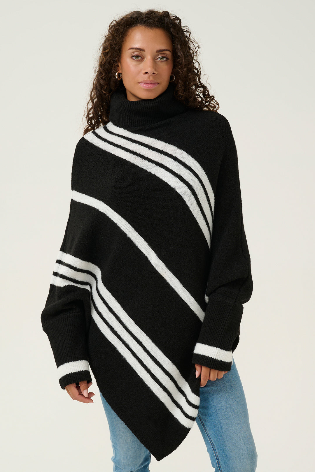 Woman wearing a black poncho with white stripes on a plain background