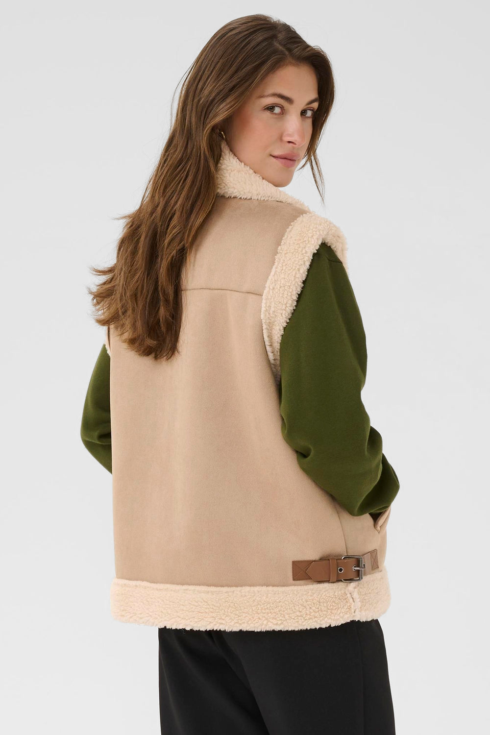 Woman wearing a beige vest with a green shirt underneath on a white background