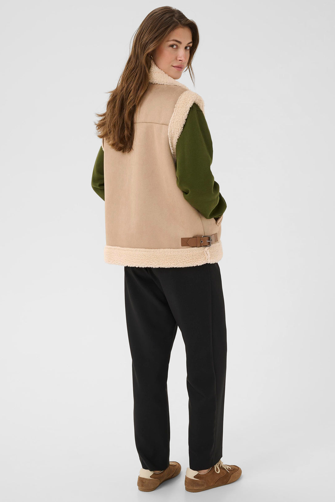 Woman wearing a beige and green jacket with black pants on a white background