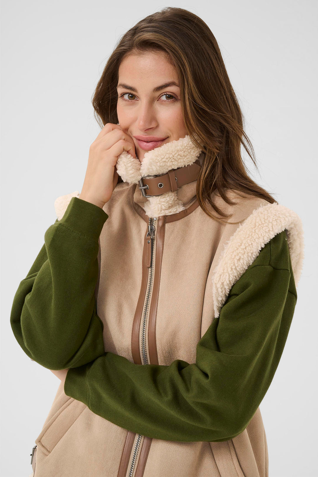 Woman wearing a green and beige jacket with a fur-lined hood on a white background