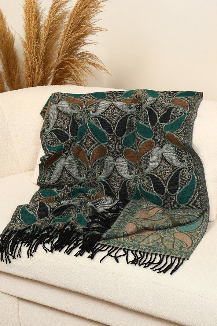 Patterned throw blanket with fringes on a white surface, with decorative elements in the background.