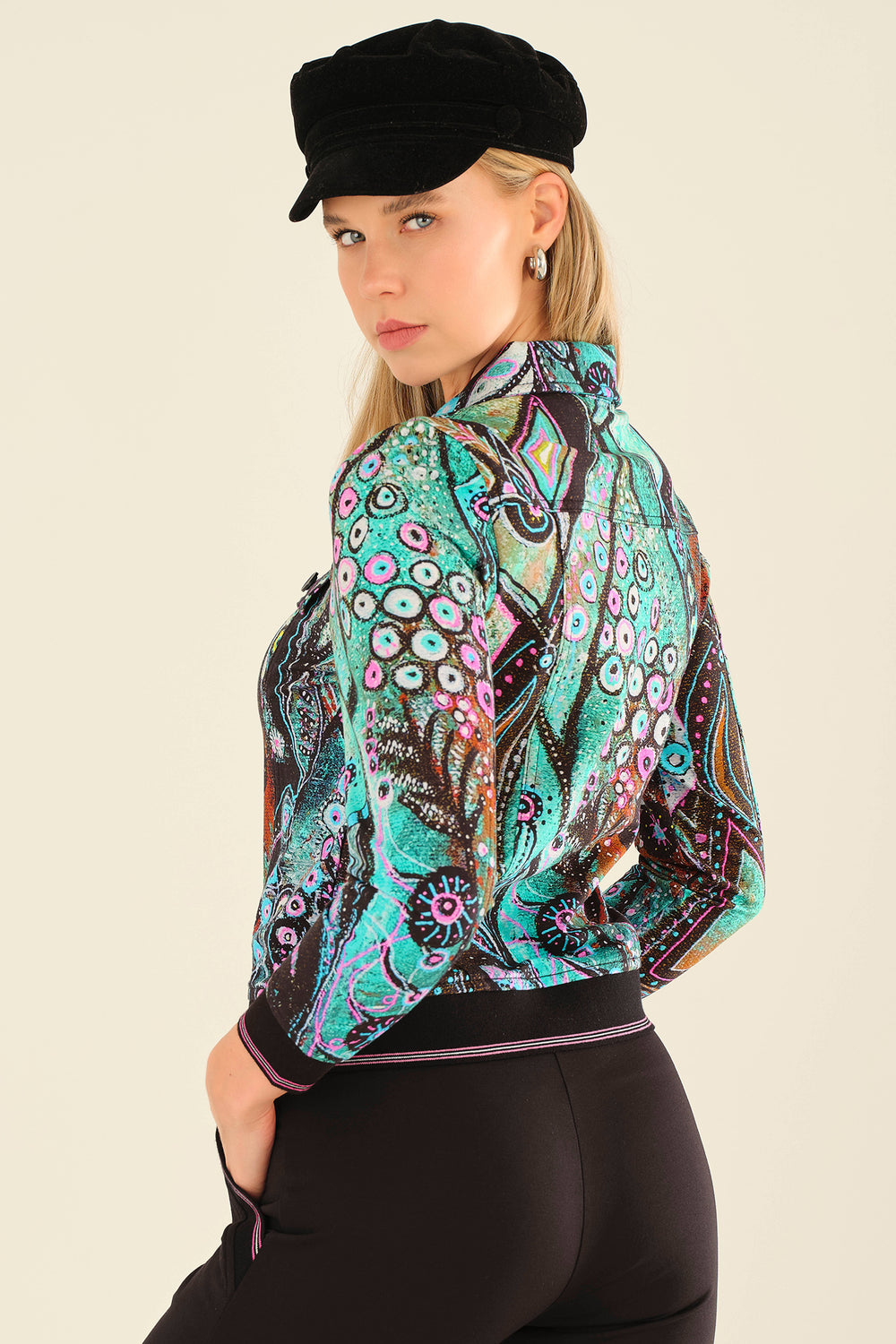 Woman wearing a colorful patterned jacket and black cap on a beige background