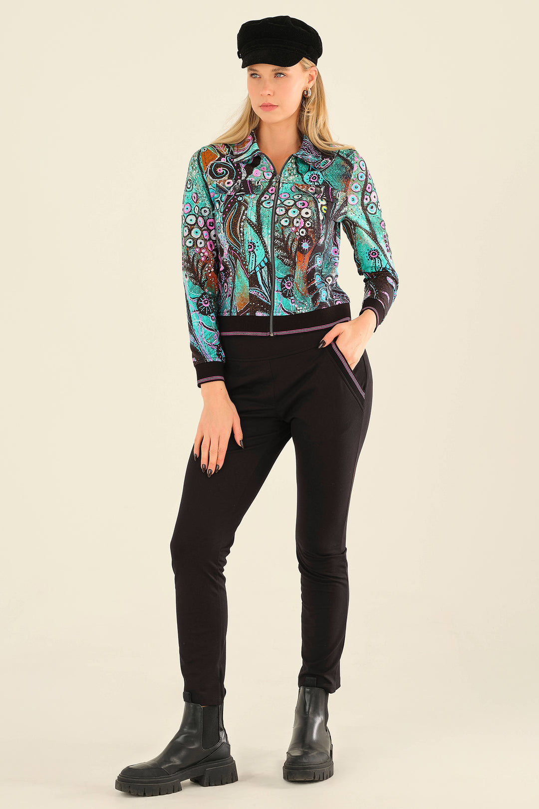 Woman wearing a colorful patterned jacket and black pants on a beige background