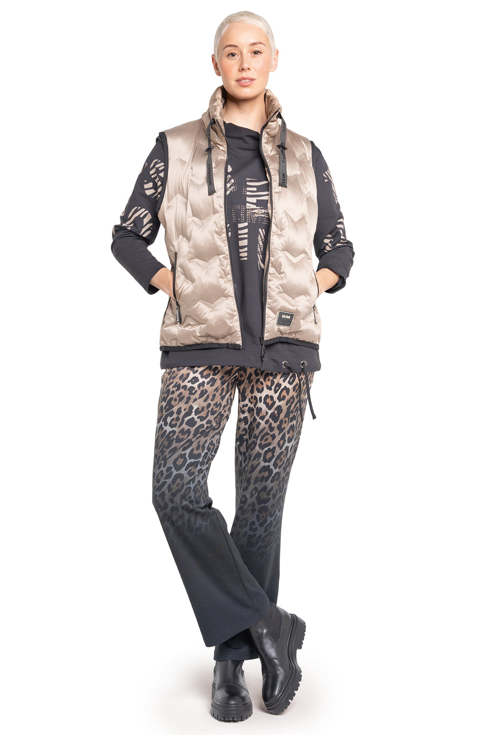 Person wearing a patterned vest, black pants with leopard print, and black boots on a white background