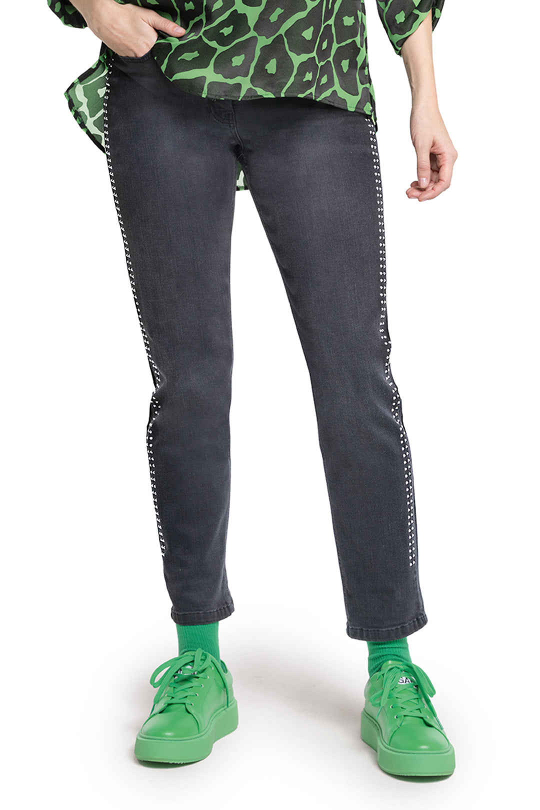 Person wearing black jeans with white stitching and green sneakers on a white background