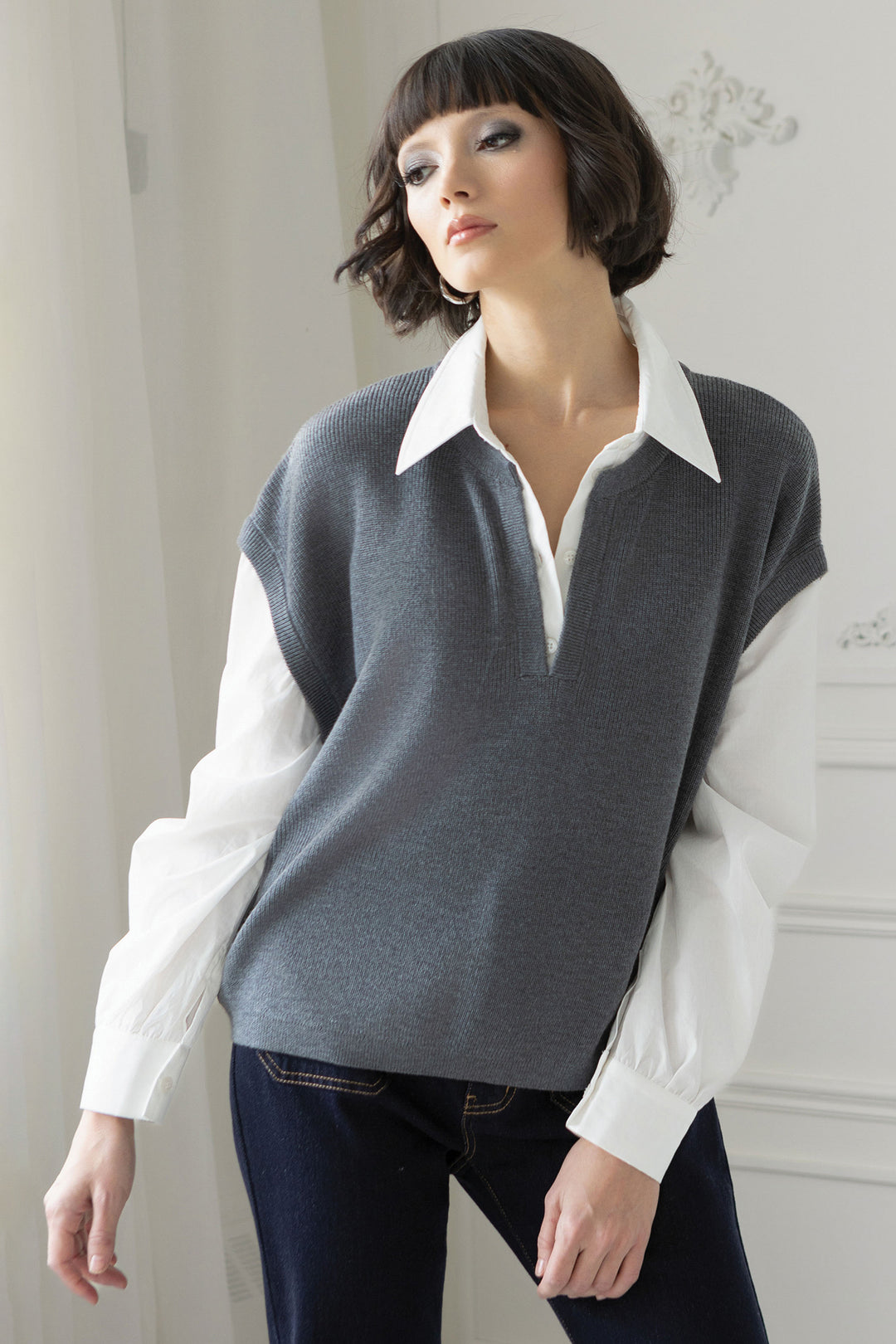 Woman wearing a gray sweater vest over a white shirt with a plain background
