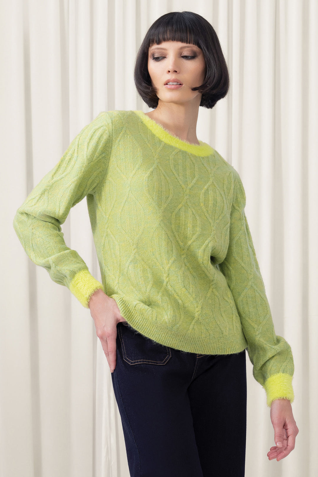 Woman wearing a green cable knit sweater against a white background