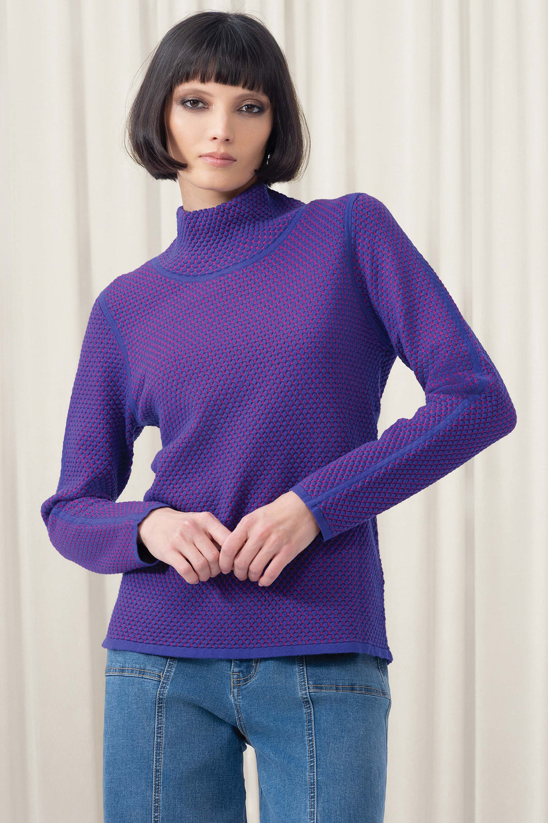 Woman wearing a purple sweater and blue jeans against a white background