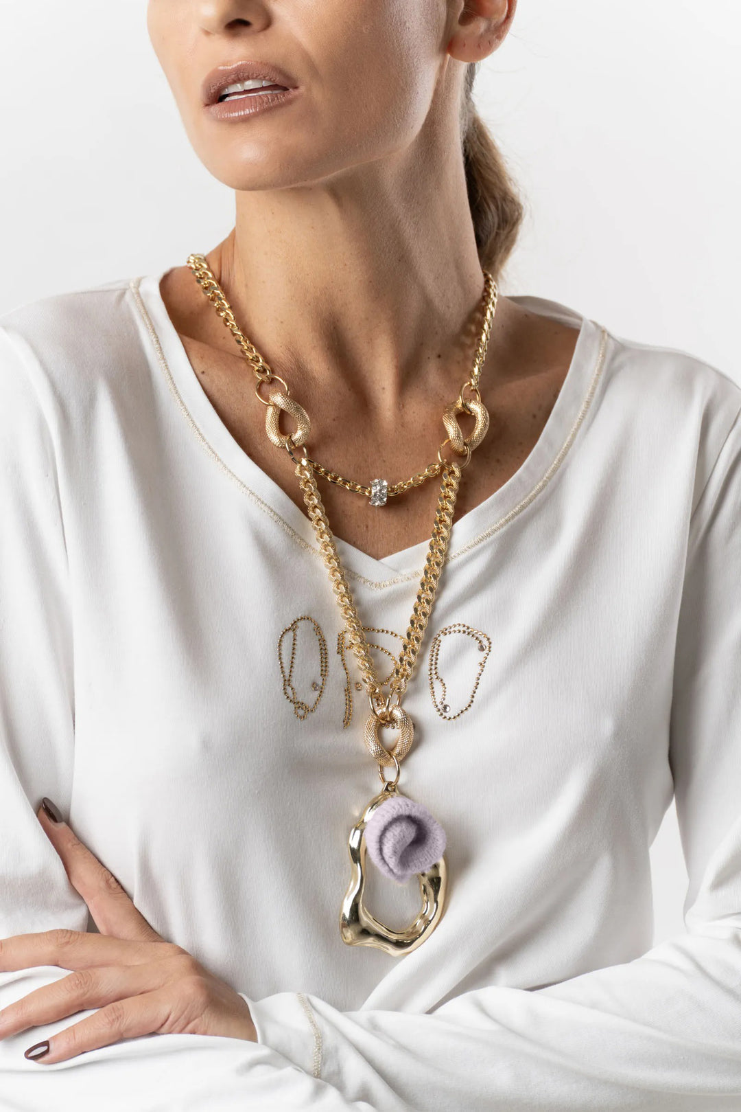 Woman wearing a white long-sleeve top with gold necklaces and a pendant.