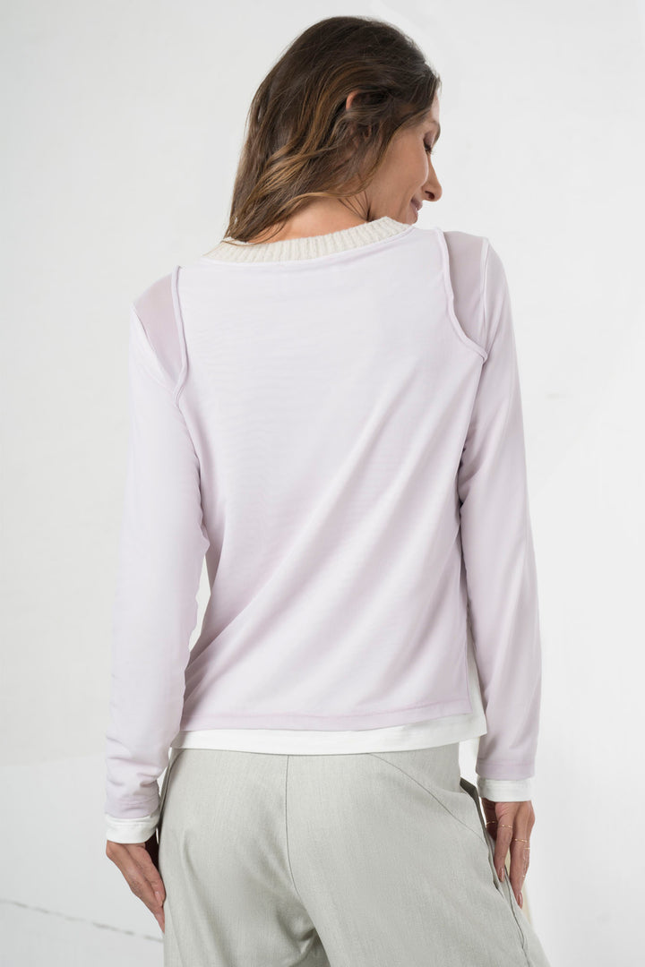 Woman wearing a light purple long-sleeve top and light gray pants on a white background