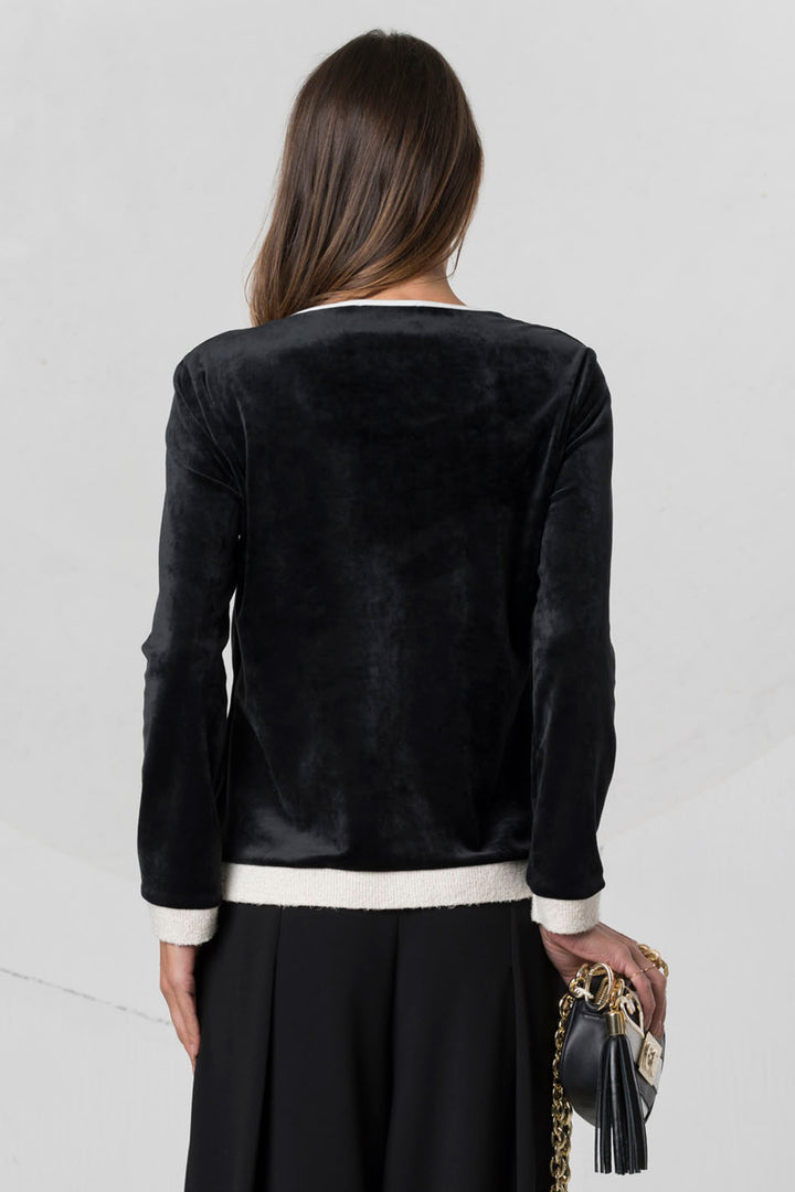 Person wearing a black velvet jacket with a white trim on a light gray background