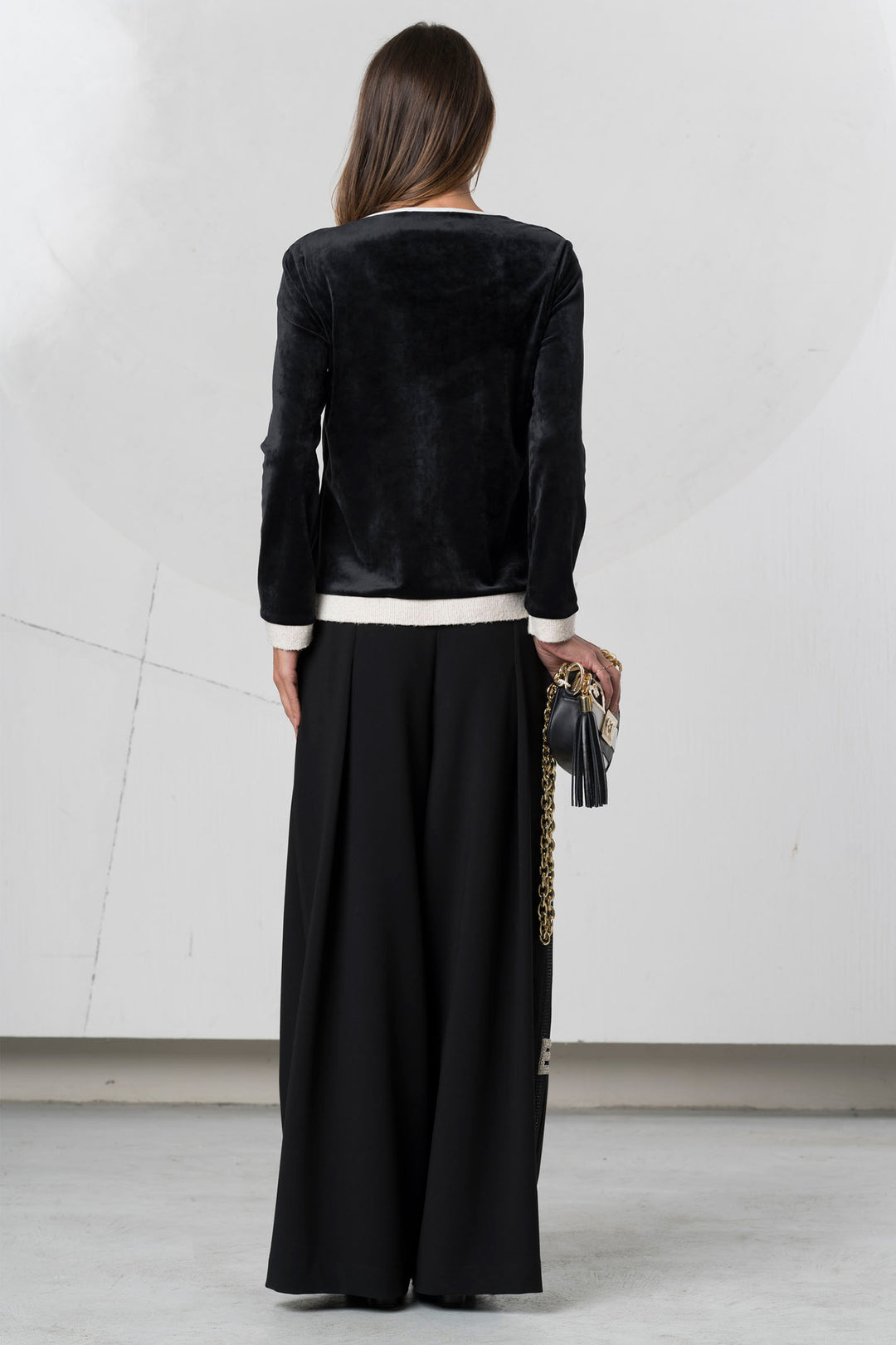 Woman wearing a black velvet jacket and black pants with a white shirt underneath, holding a clutch.
