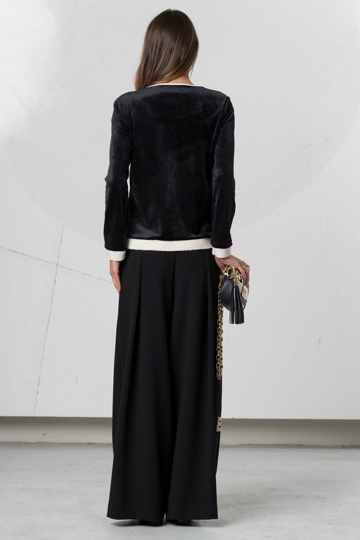 Woman wearing a black velvet jacket and black pants with a white shirt underneath, holding a clutch.