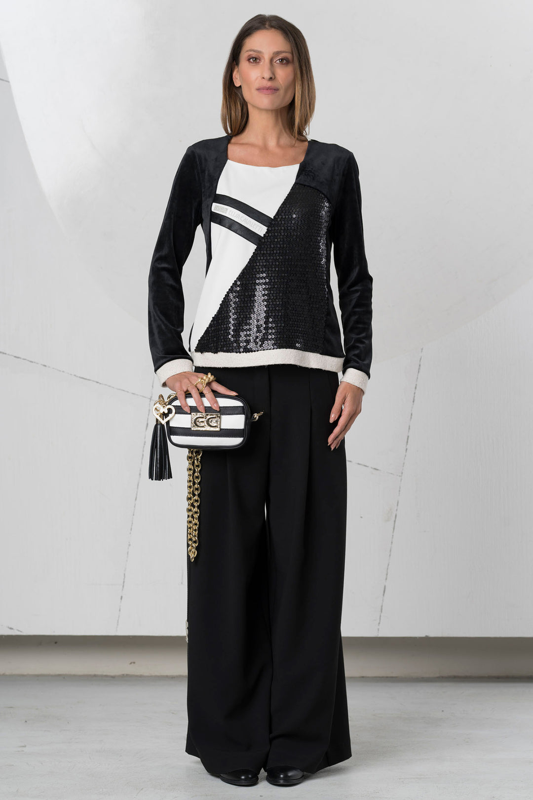 Woman wearing a black and white outfit with a sequined top and wide-leg pants, holding a striped handbag.