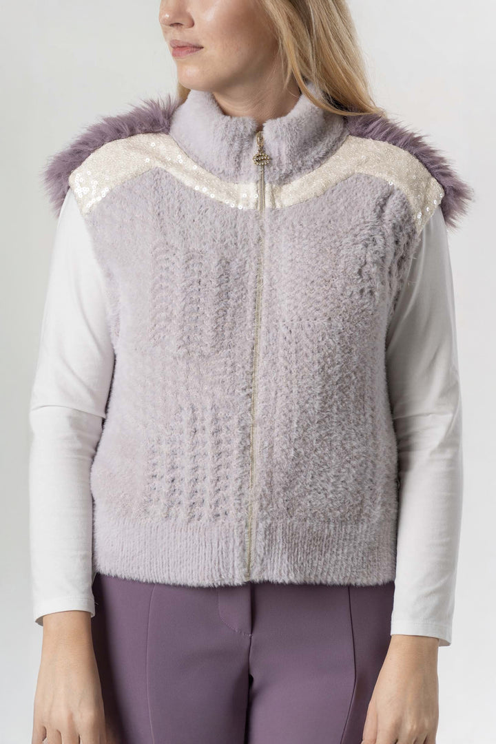 Woman wearing a light purple knitted vest with fluffy trim on a plain background