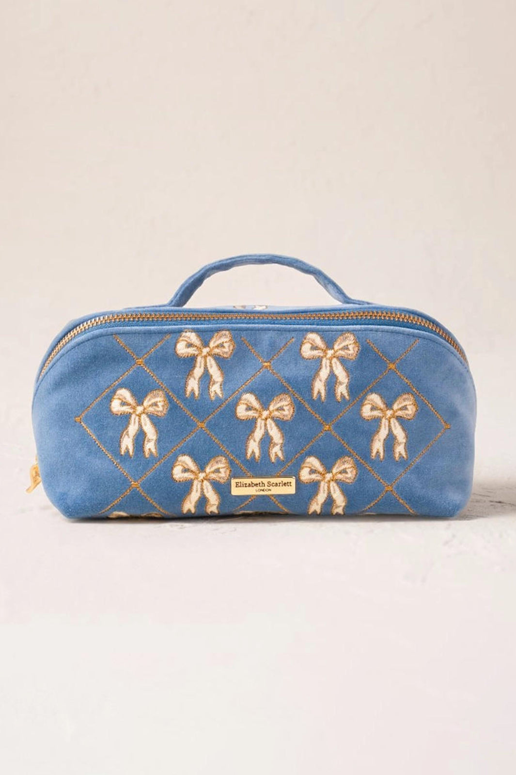 Blue cosmetic bag with gold bow patterns on a beige background