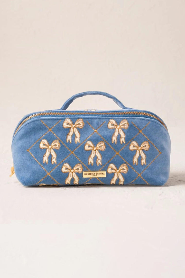 Blue cosmetic bag with gold bow patterns on a beige background