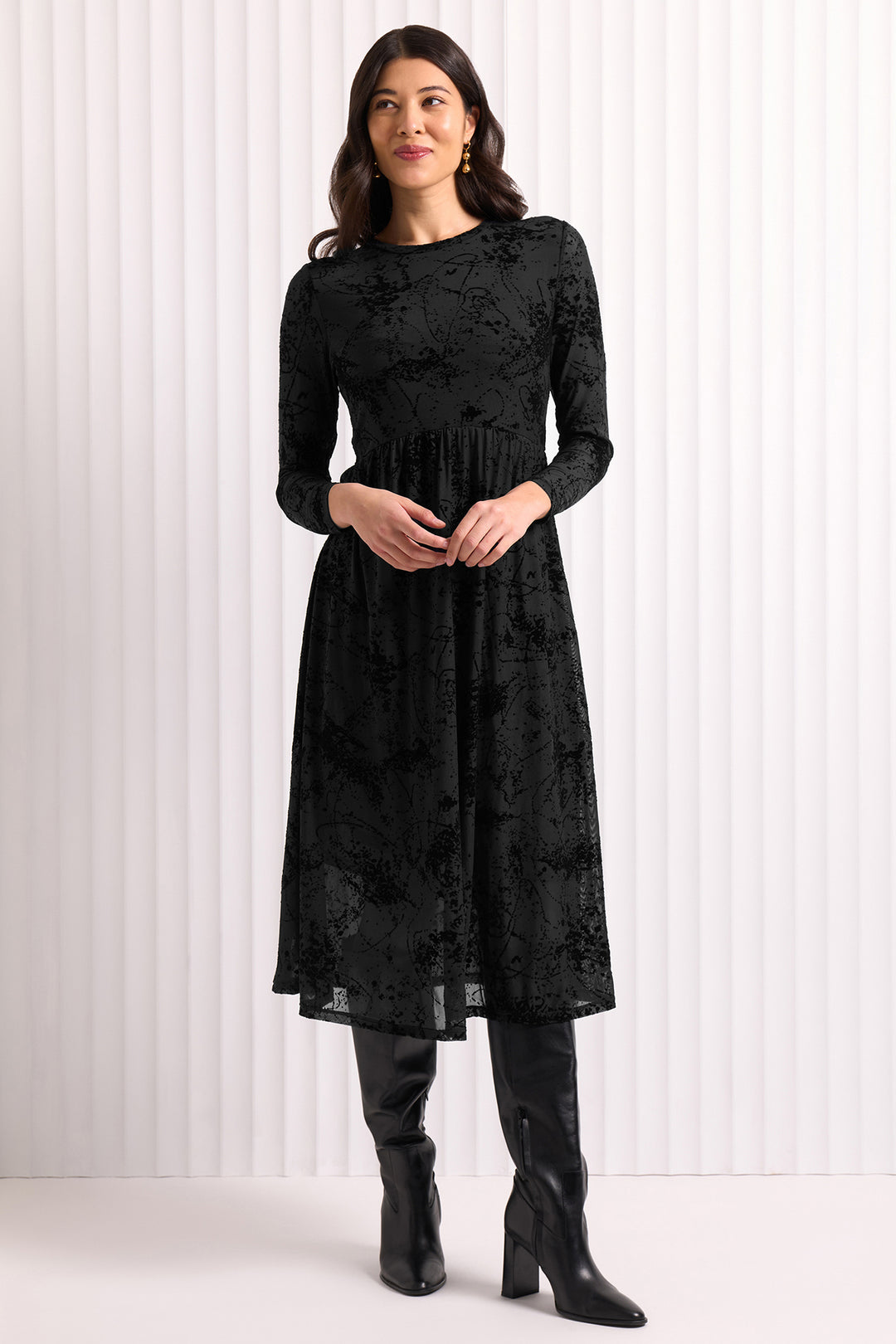 Woman wearing a black lace dress with long sleeves against a white background