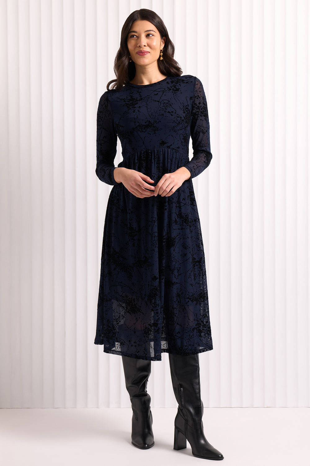Woman wearing a navy lace dress with black boots against a white background