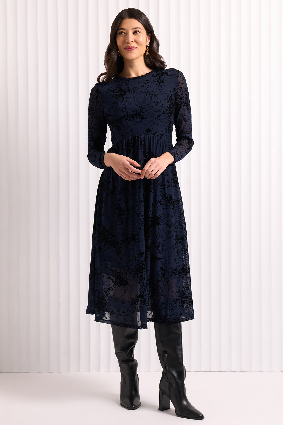 Woman wearing a navy lace dress with black boots against a white background
