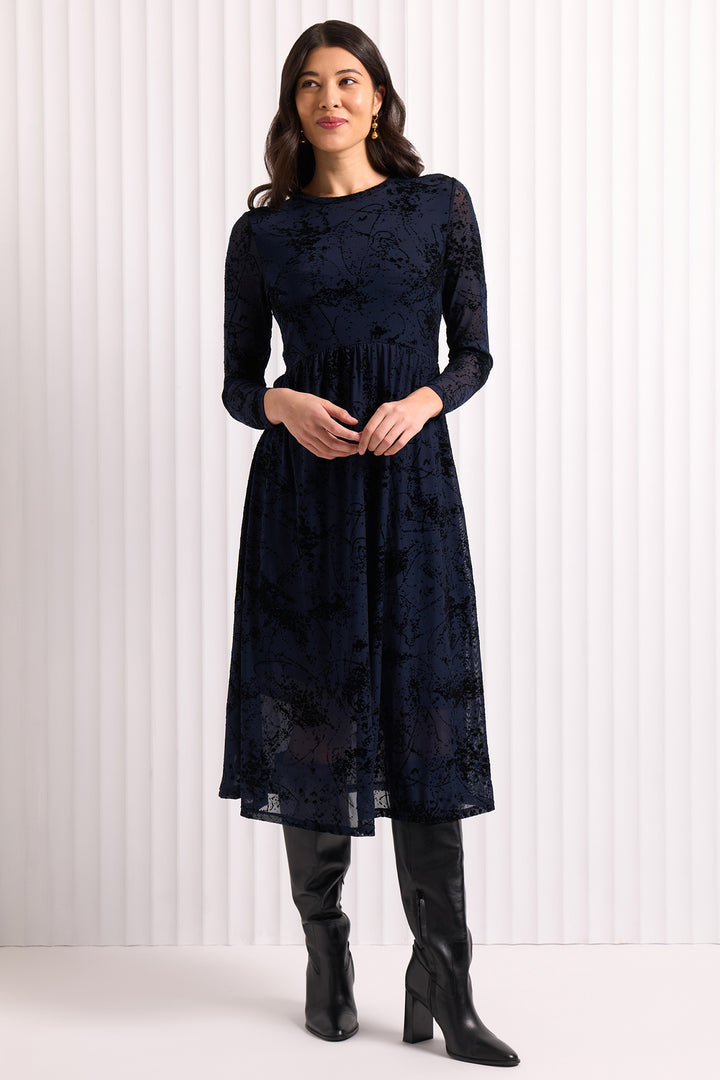 Woman wearing a navy lace dress with black boots against a white background