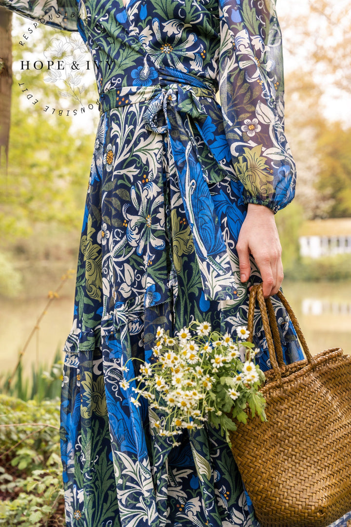 Person wearing a floral dress holding a woven bag and flowers outdoors.