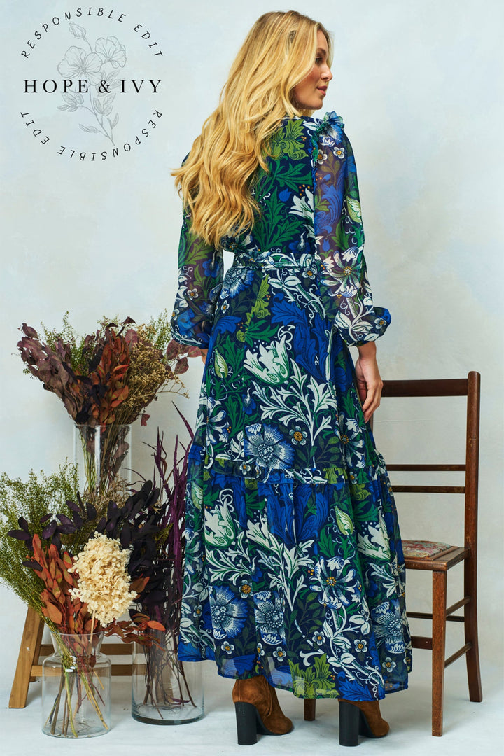 Woman in a floral dress standing next to a wooden chair and vase of flowers, with 'Hope & Ivy' branding.