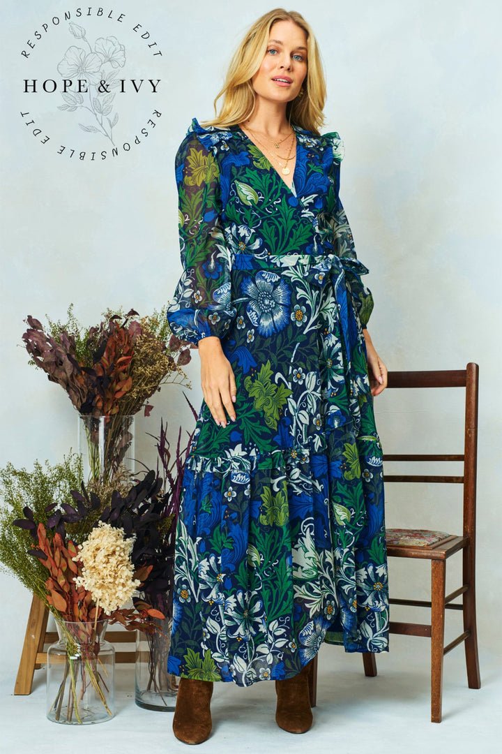 Woman wearing a floral dress with dried plants and a chair in the background, featuring the 'Hope & Ivy' brand.