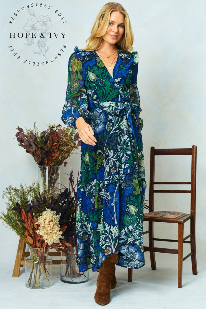 Woman wearing a blue floral dress with dried flowers and a wooden chair in the background, featuring the brand 'Hope & Ivy'.