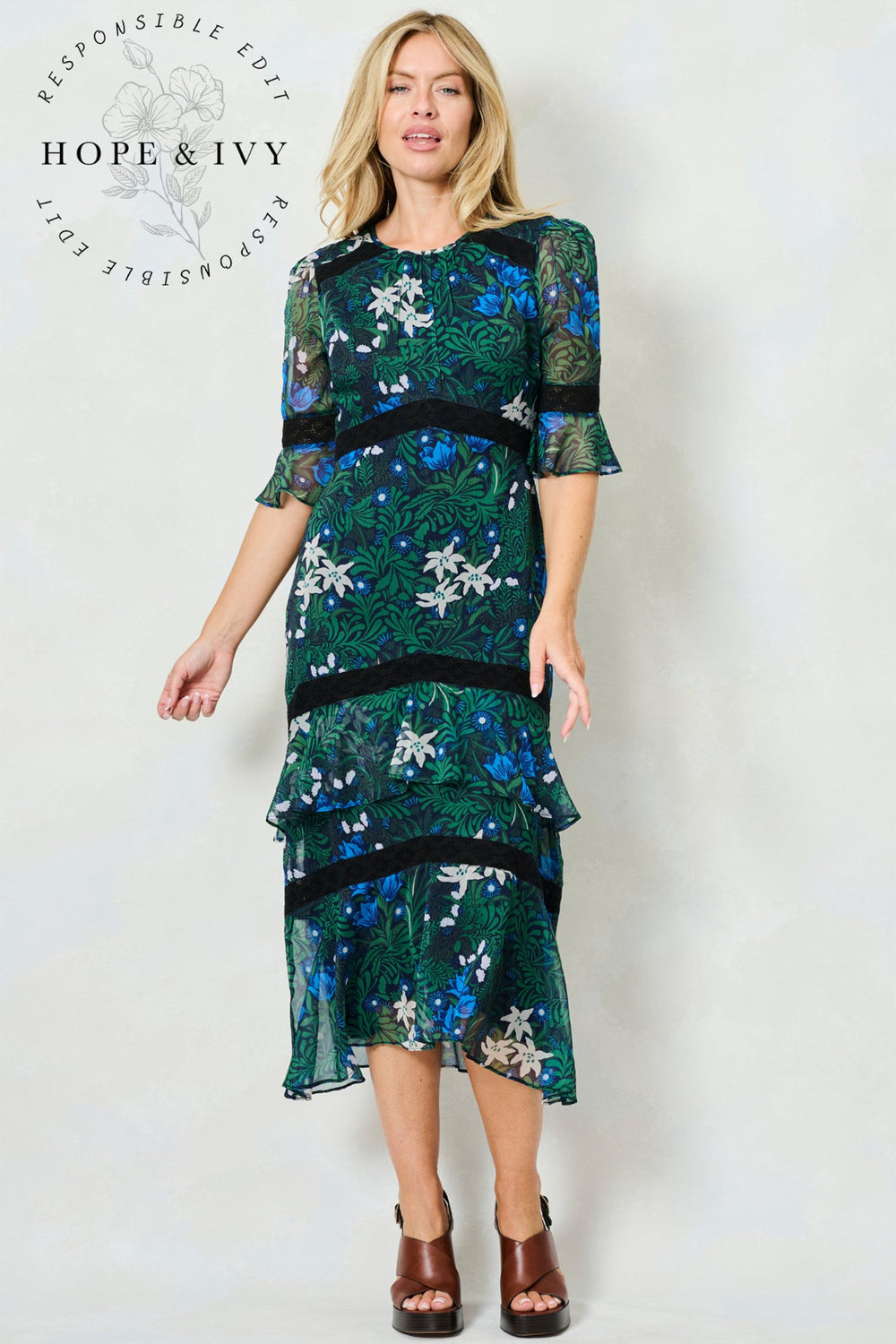 Woman wearing a green floral dress with 'Hope & Ivy' branding on a white background