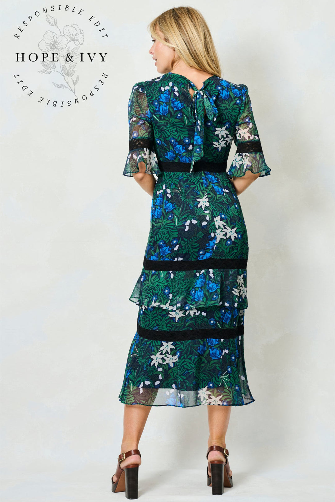 Woman wearing a green and blue floral dress with 'Hope & Ivy' branding.