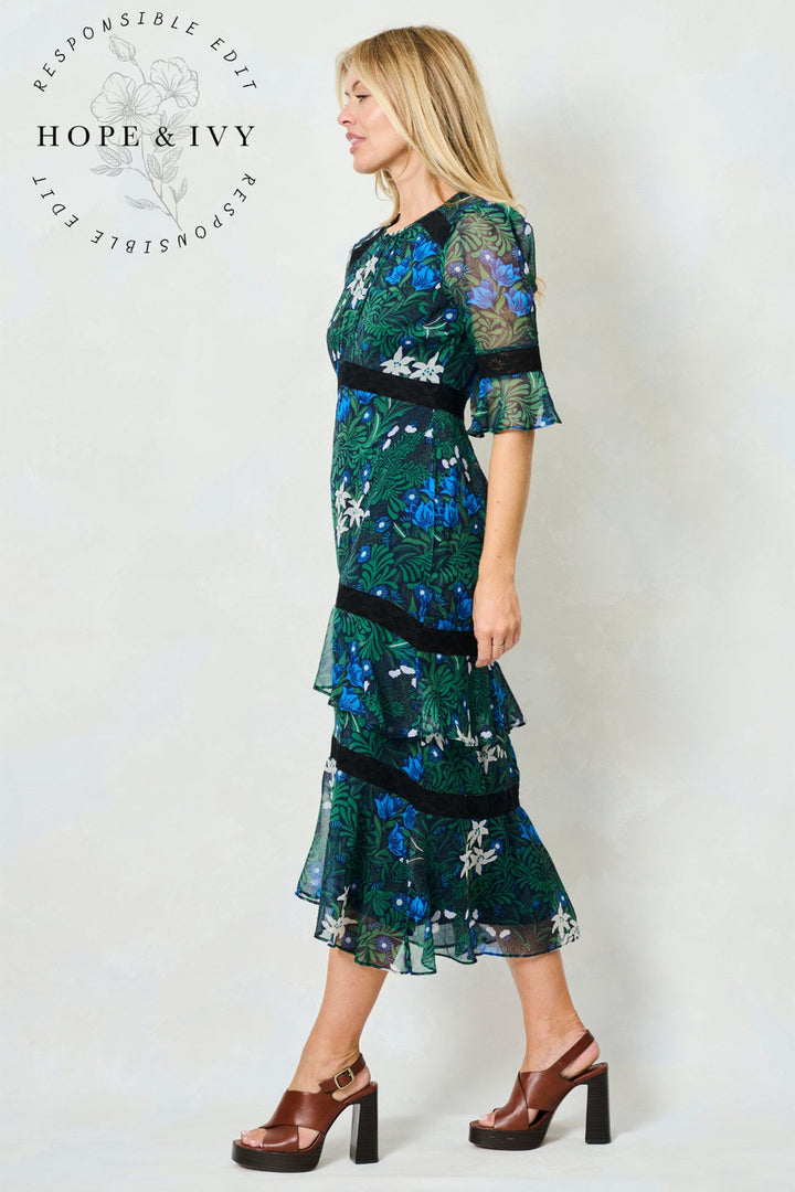 Woman wearing a green and blue patterned dress with 'Hope & Ivy' branding.